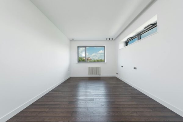 Interior of empty spacious room with white walls and brawn parquet floor in daylight