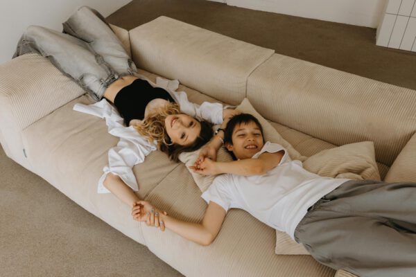 Young woman and boy relaxing on a modern beige sofa, enjoying time indoors.