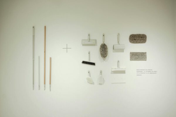 A minimalist flat lay of various cleaning tools arranged on a white wall, showcasing a modern concept.