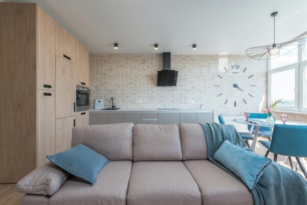 Minimalistic interior design of modern light studio consisting of big sofa and kitchen with dining table and chairs against brick wall in da