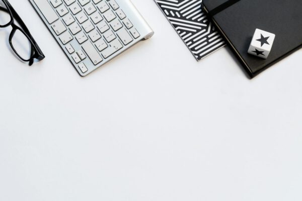A stylish home office flat lay with a keyboard, glasses, and notebooks on a white backdrop.
