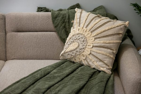 Comfortable beige couch with decorative boho pillow and green throw, perfect for a cozy interior setting.