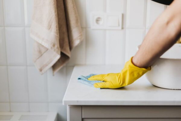 Crop anonymous woman in yellow protective gloves cleaning surface of cabinet near sink in bathroom during housework