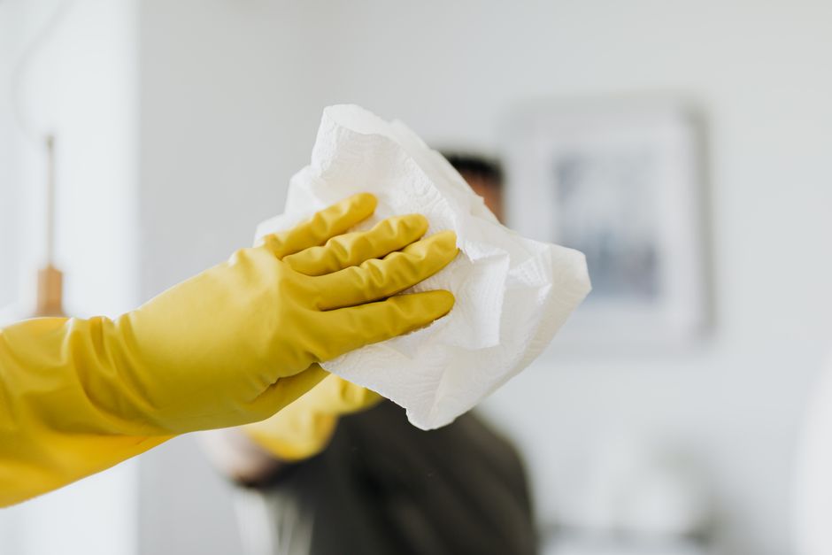 Faceless male wearing yellow latex gloves and wiping mirror with paper napkin in bathroom while cleaning and disinfects house