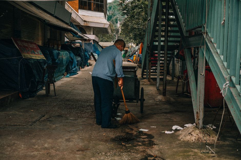 A man cleaning an urban alley in Thành phố Lạng Sơn, Việt Nam with a broom.