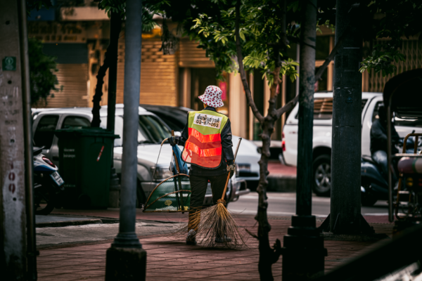 Street sweeper working on a sidewalk in Bangkok, Thailand, with a broom and dustpan.